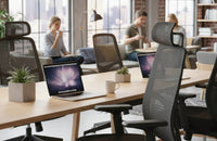 Sillas de oficina ergonómicas con respaldo de malla negra rodeando una mesa colaborativa de madera con ordenadores portátiles.