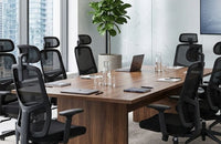 Sillas ergonómicas de malla negra dispuestas alrededor de una gran mesa de reuniones de madera en una sala de juntas corporativa.